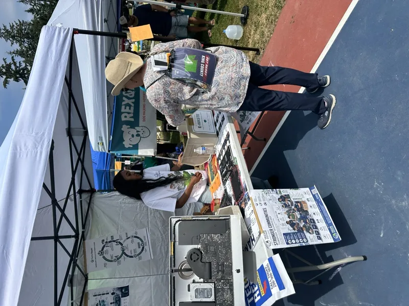 Techs Repair outreach booth with disassembled iMac and e-waste collection box at a community event